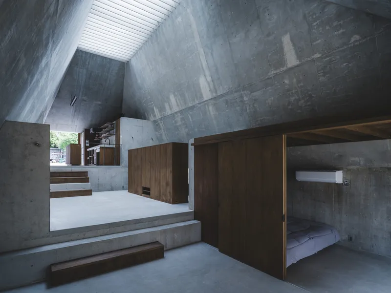 Split-level interior with concrete steps and timber sleeping alcove beneath a slatted skylight