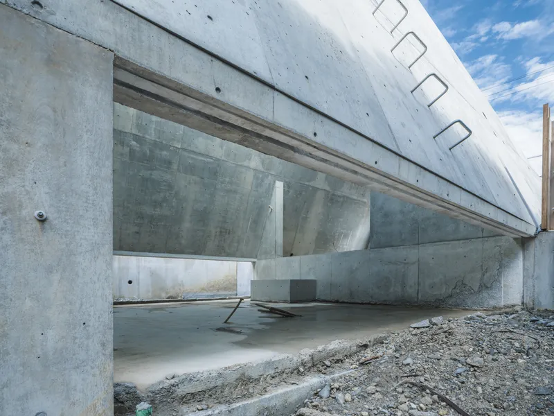 Angled concrete soffit with continuous clerestory glazing above exposed gravel and construction site