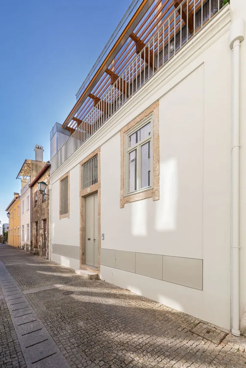 Street view showing white rendered facade with stone-framed door and timber pergola addition above