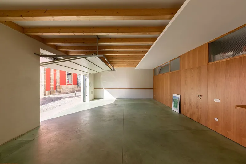 Open garage space with exposed timber beams and polished concrete floor opening to red striped facade