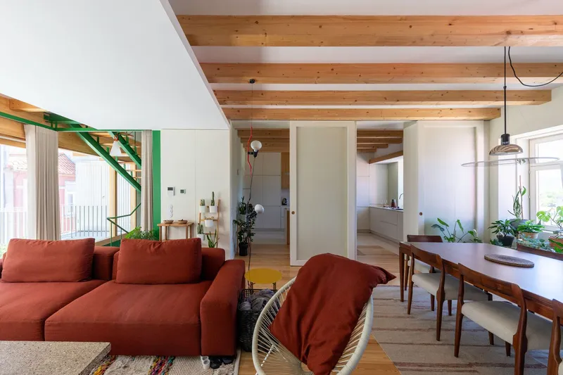 Living and dining area with green steel staircase and exposed timber ceiling beams with potted plants