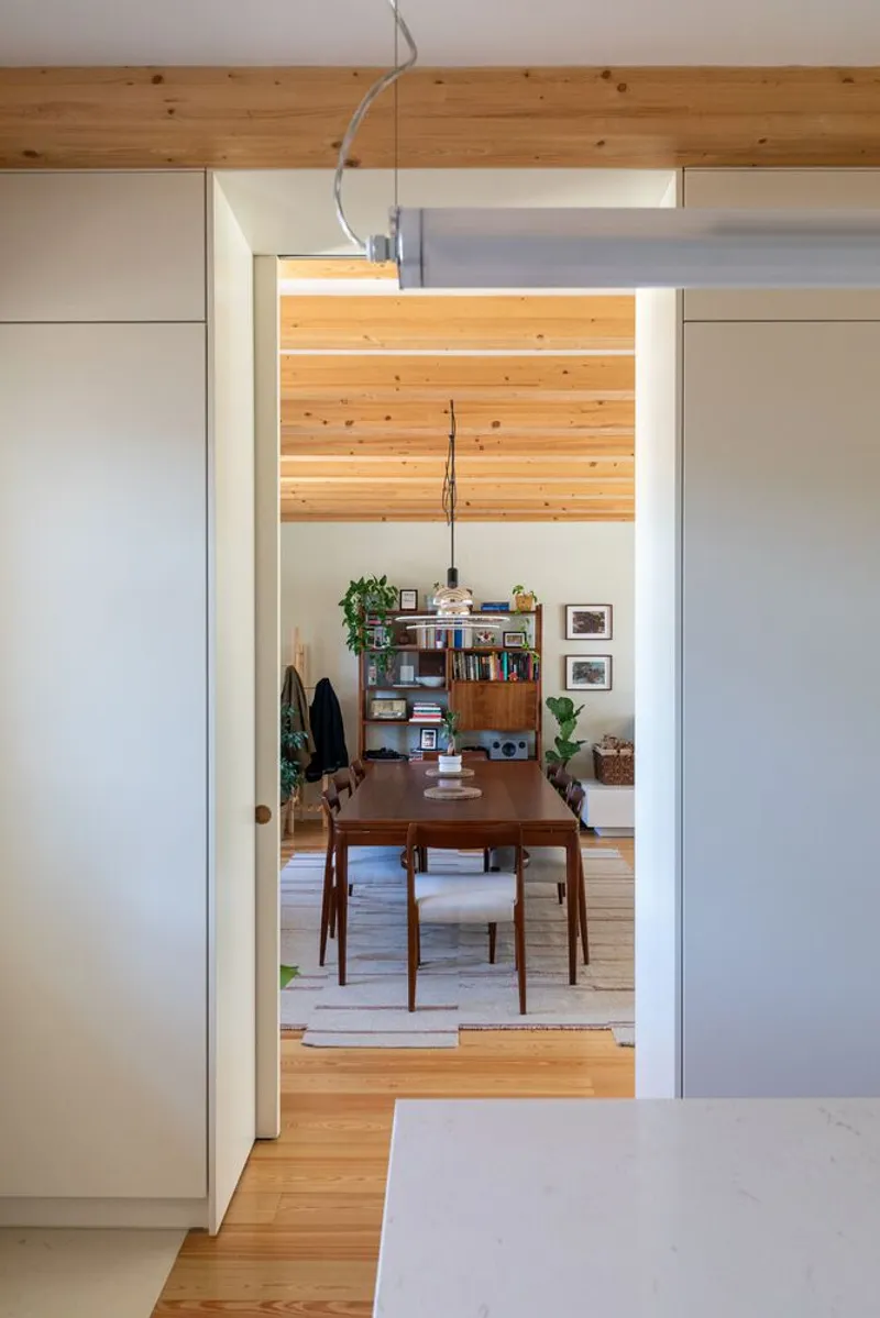 View through white-framed doorway to dining room with exposed timber ceiling and wood flooring