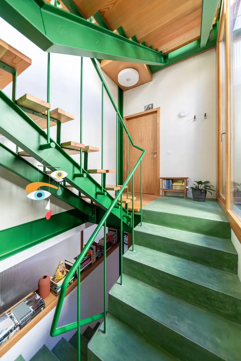 Double-height entry hall with green steel staircase, wood treads, and green carpeted floor platform