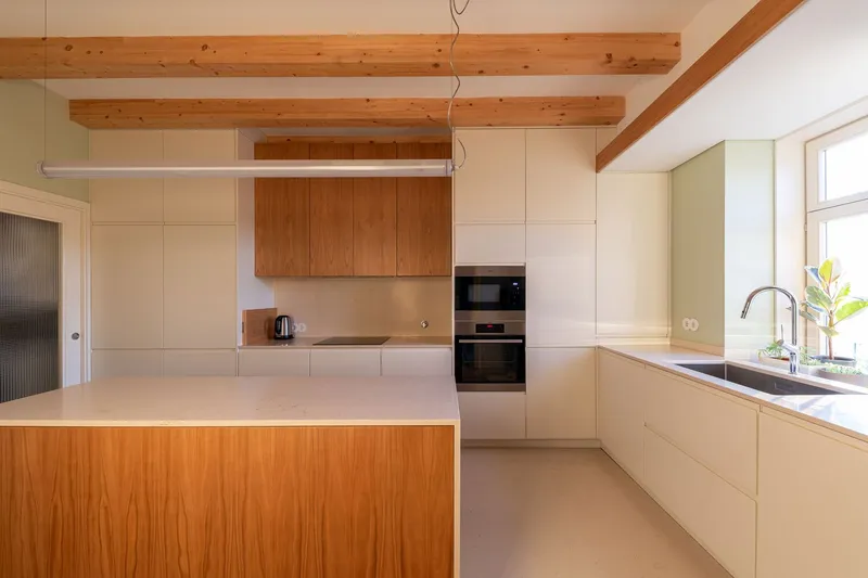 Kitchen with pale wood cabinetry, exposed timber ceiling beams, and a central island with wood panel front