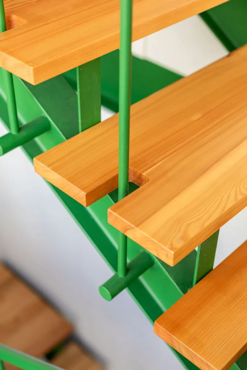 Close-up of timber treads with green steel supports threaded by a vertical green handrail