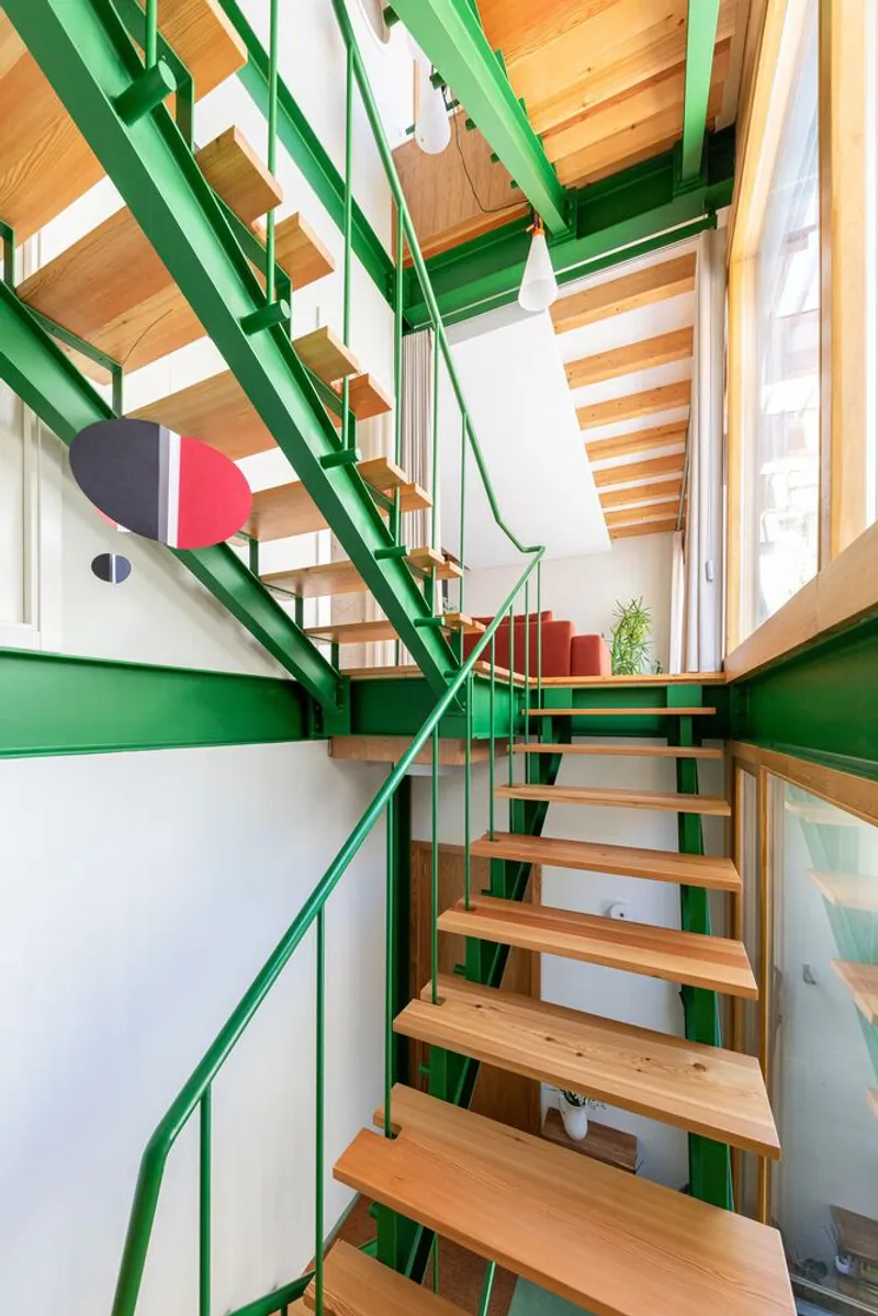 Upward view of open-tread staircase with green steel frame under exposed timber ceiling joists