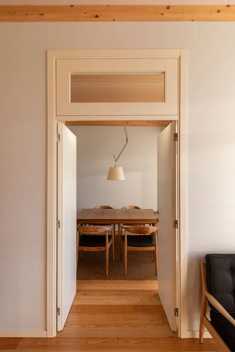 View through an open doorway with cane transom panel toward a timber dining table under a pendant lamp