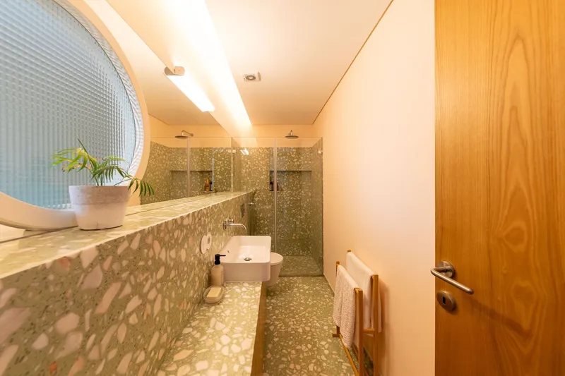 Bathroom with terrazzo floor and walls, glass shower enclosure, and circular textured glass window above the vanity