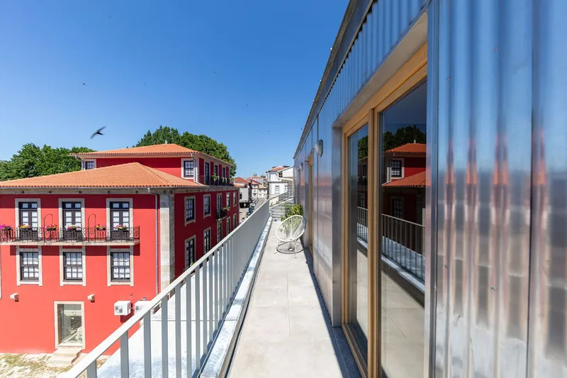 Rooftop terrace with corrugated metal balustrade and glazed sliding doors reflecting the adjacent red tile-roofed building