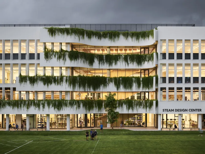 White facade with cascading greenery across recessed balconies lit from within at dusk