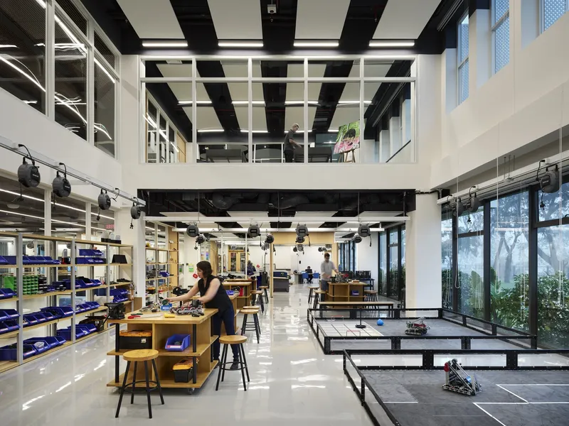 Double-height workshop space with exposed black ceiling structure and full-height glazing overlooking greenery