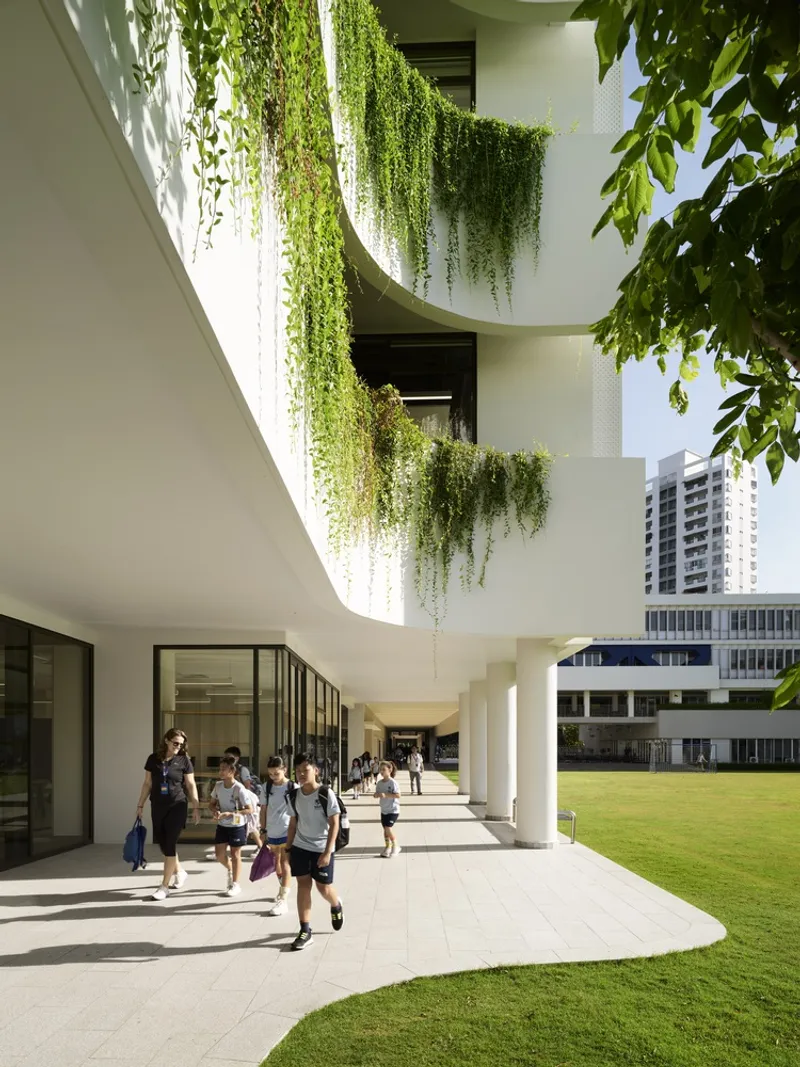 Covered walkway with white columns and trailing plants overhead as students pass through bright midday sun