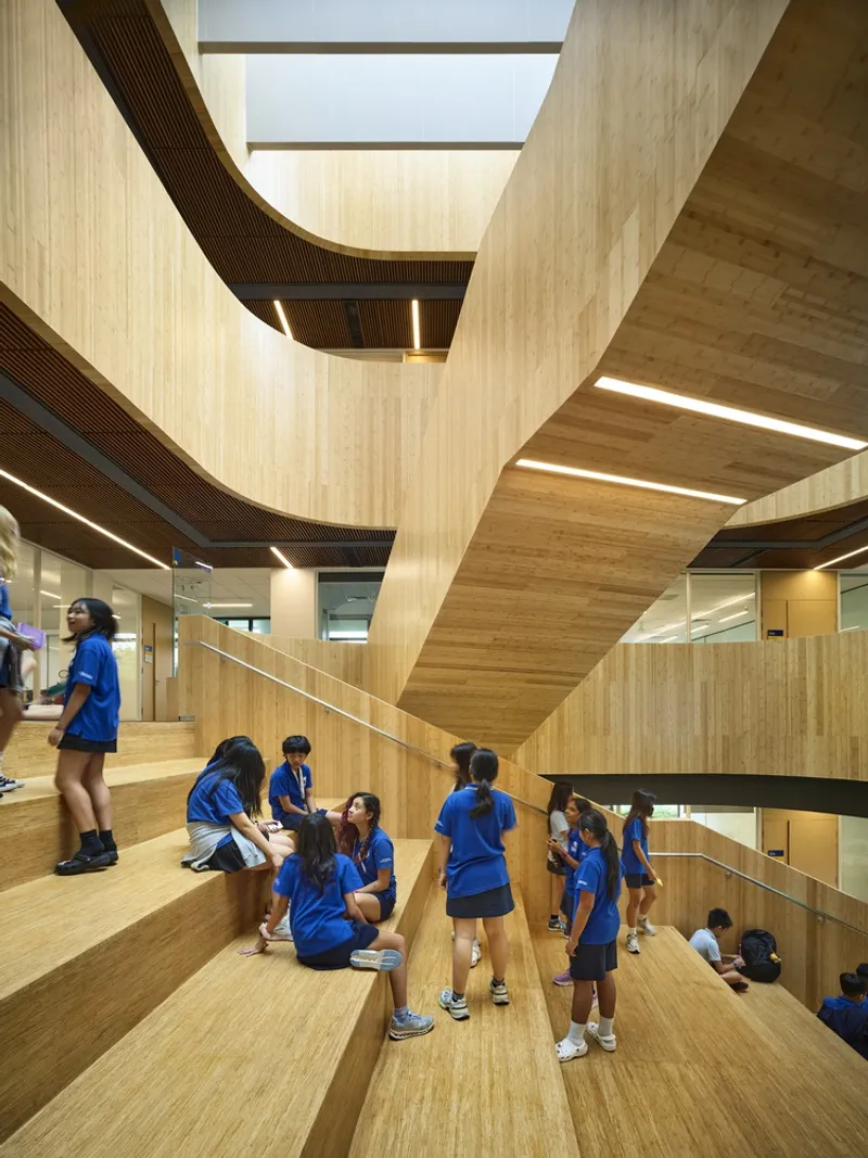 Wide timber staircase with integrated seating where students gather beneath curved wood-clad ceilings and skylights