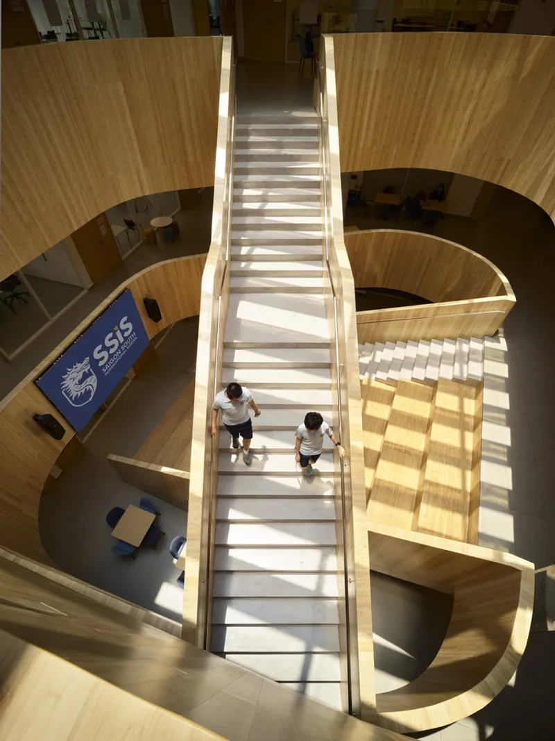 Top-down view of the central timber staircase with sunlight casting shadows and two people ascending