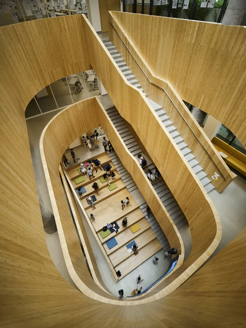 Multi-story atrium with nested timber-clad oval stairways and students seated on stepped platforms