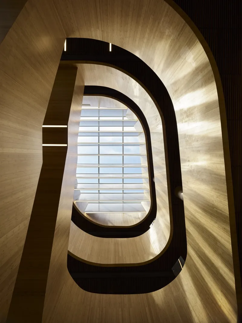 Looking up through the rounded wood-lined stairwell with black handrails and skylight above