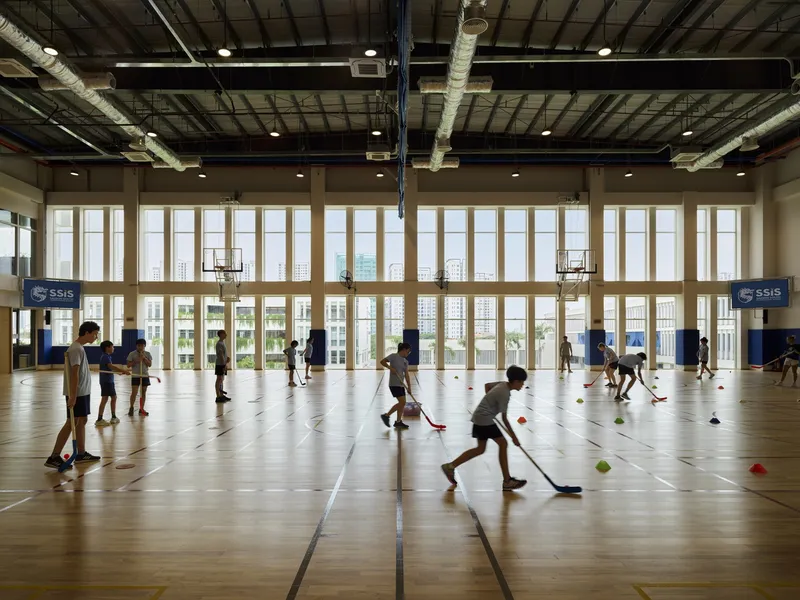 Gymnasium interior with children playing floor hockey under exposed ceiling beams and full-height windows