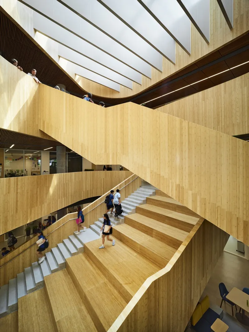 Wide timber staircase with students ascending beneath angled skylights and ribbed wood soffit