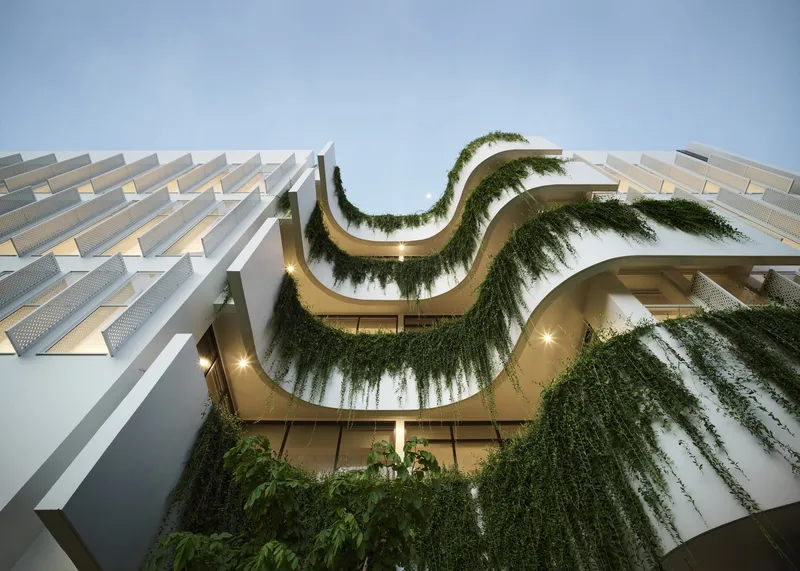 Facade detail showing stacked vegetated terraces between white louvered panels at dusk