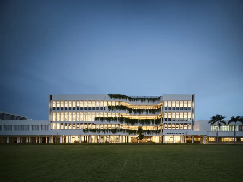 Illuminated facade with horizontal planted terraces centered on lawn at dusk