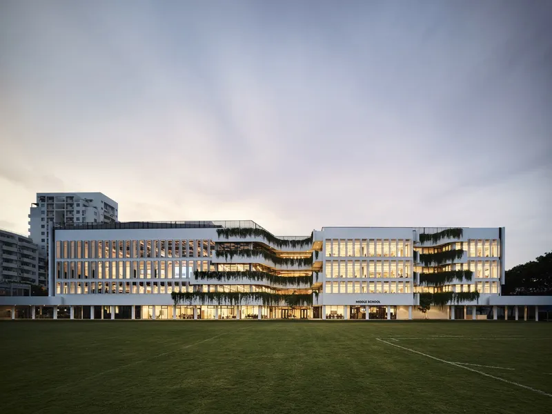 Campus facade with vertical louvers and planted terraces facing a grass playing field at dusk