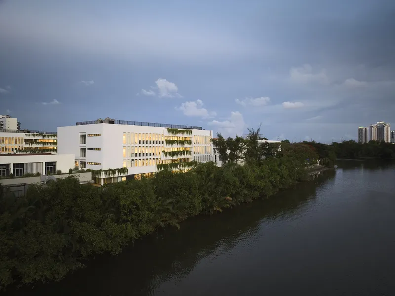 White volumes with vertical sunscreens and planted balconies rising above a mangrove waterway