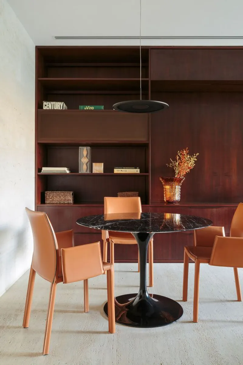 Dining nook with black marble tulip table and leather chairs against built-in mahogany shelving