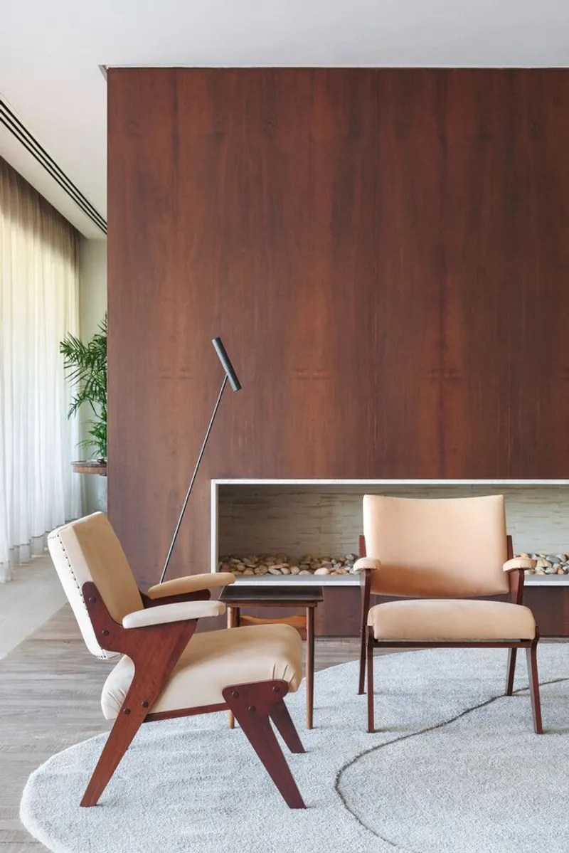 Pair of upholstered lounge chairs beside a mahogany wall with recessed fireplace and illuminated niche