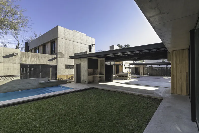 Private courtyard with lawn and swimming pool enclosed by board-formed concrete walls under clear sky