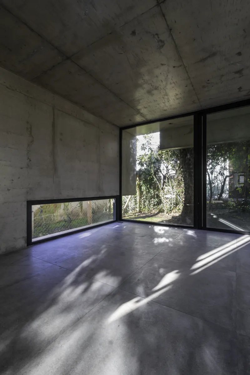 Corner room with horizontal window slot and dappled sunlight casting shadows across the floor