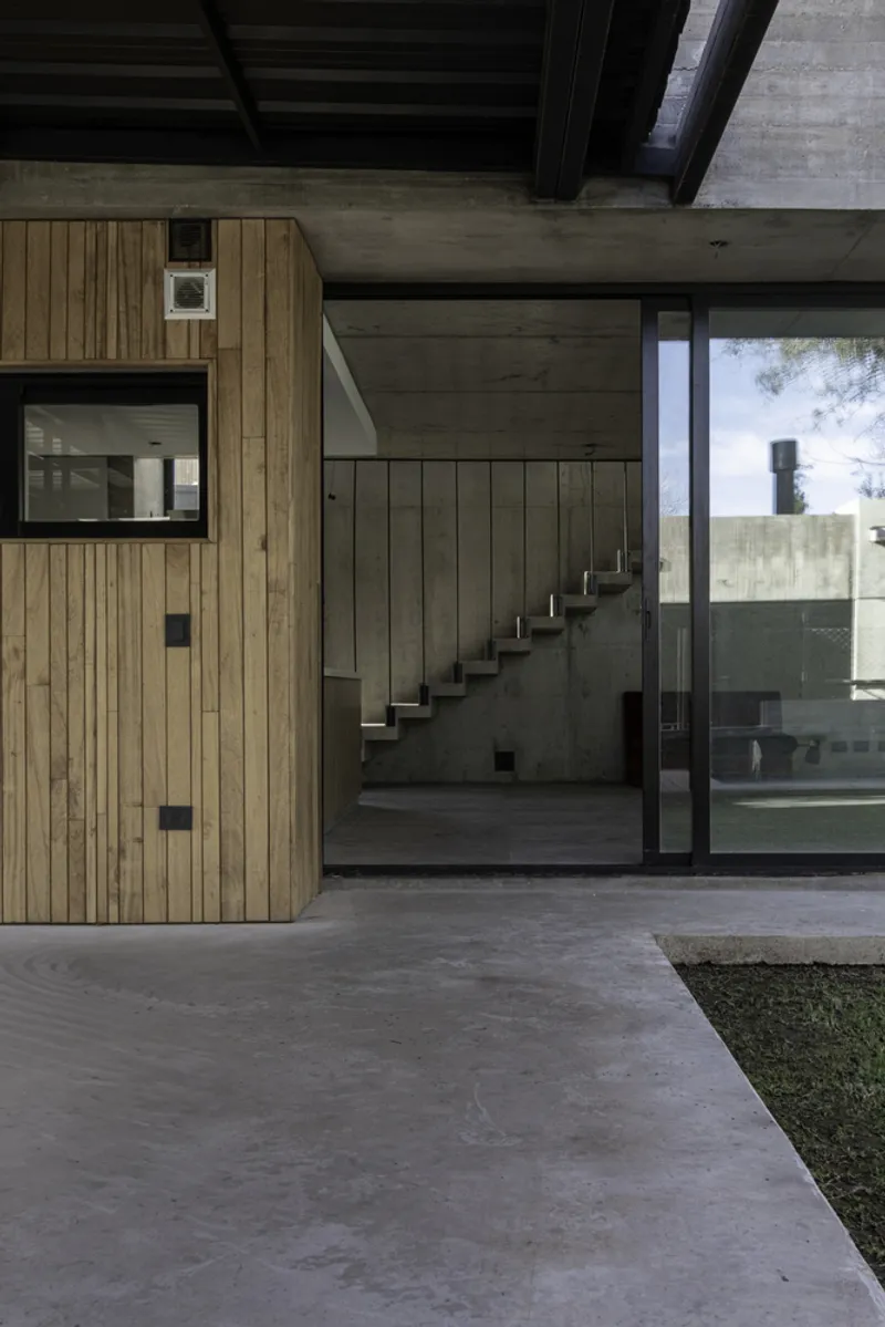 Glass-walled entry corridor revealing an internal concrete staircase with timber cladding and exposed ceiling