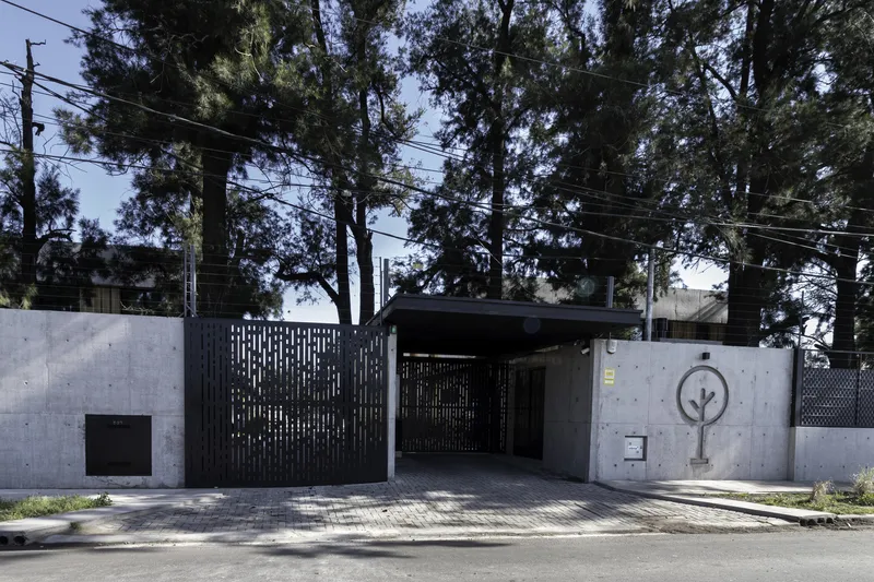 Street facade with perforated black metal gate and concrete wall set among tall evergreen trees and overhead wires