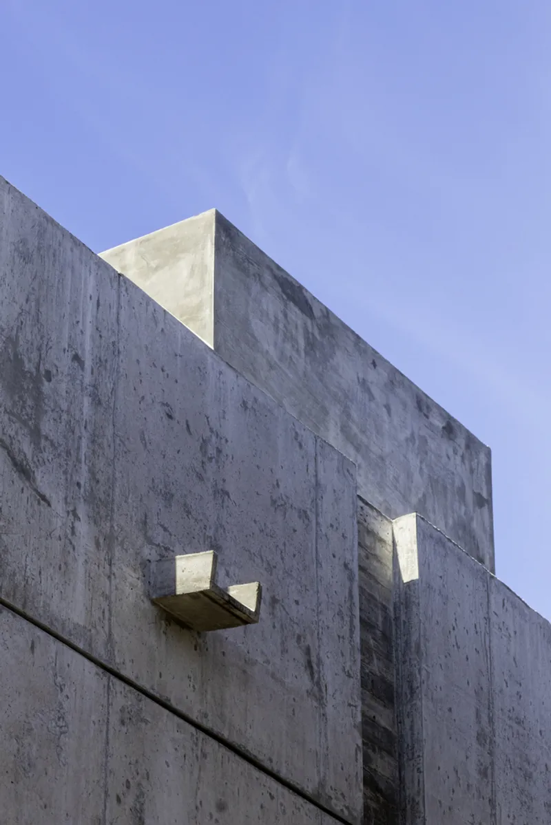Upward view of the boardformed concrete facade with triangular cutouts against a clear blue sky