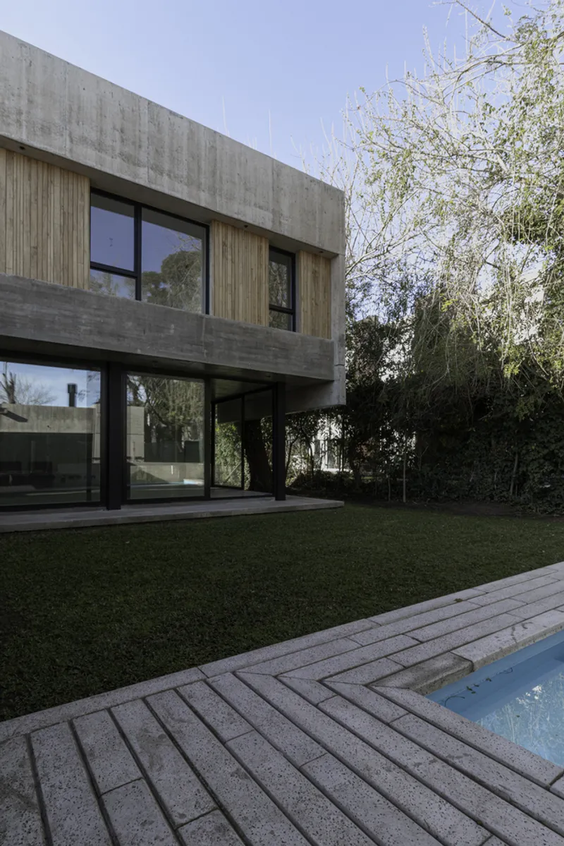 Garden view showing elevated concrete volume on black columns above lawn with timber deck and pool