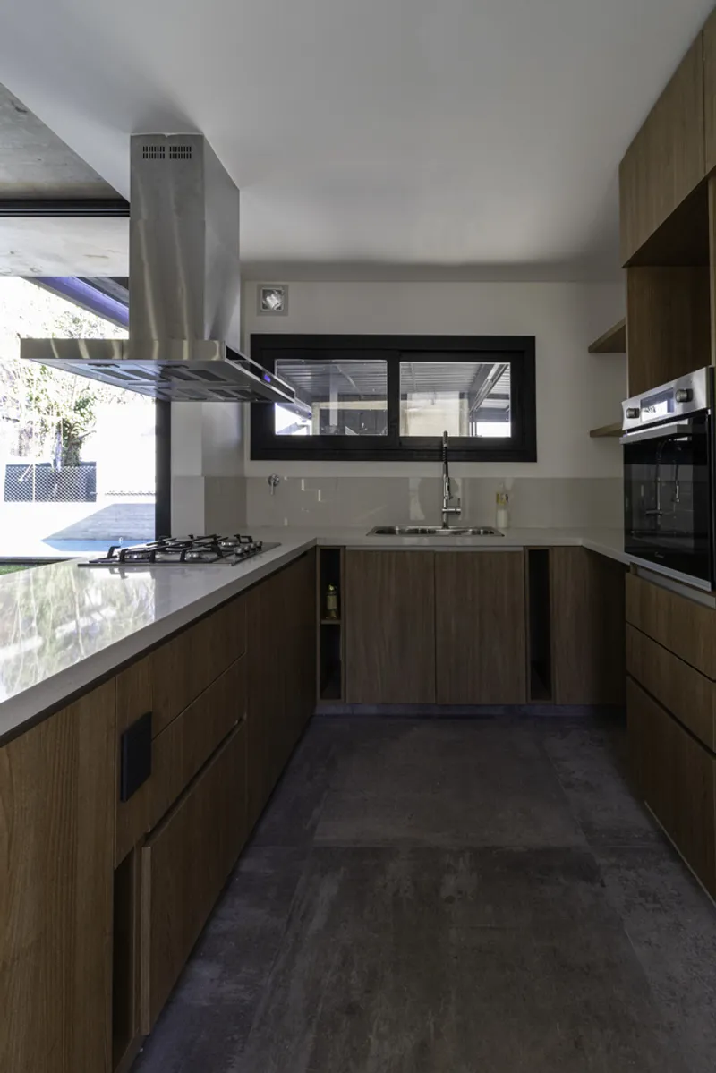 Galley kitchen with stainless steel range hood and timber veneer base cabinets under a horizontal window