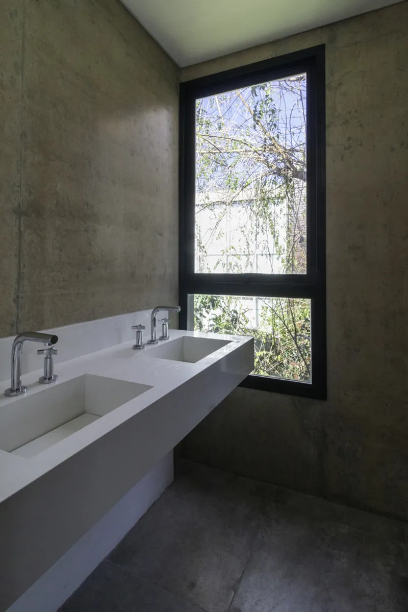 Bathroom with double concrete vanity and vertical window framing tree branches beyond