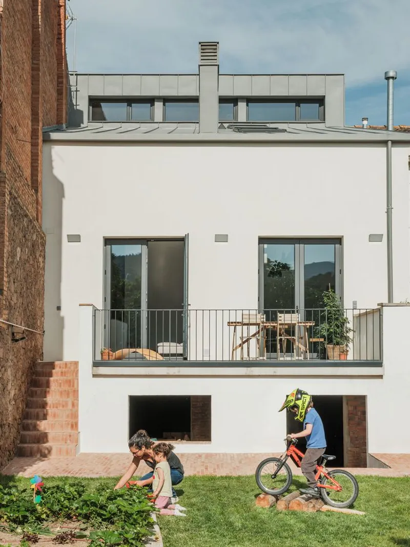 White rendered rear facade with balcony and rooftop terrace while children play in the garden below