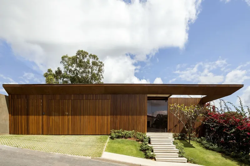 Horizontal timber-clad volume with flat overhanging roof and stepped stone pathway through planted lawn
