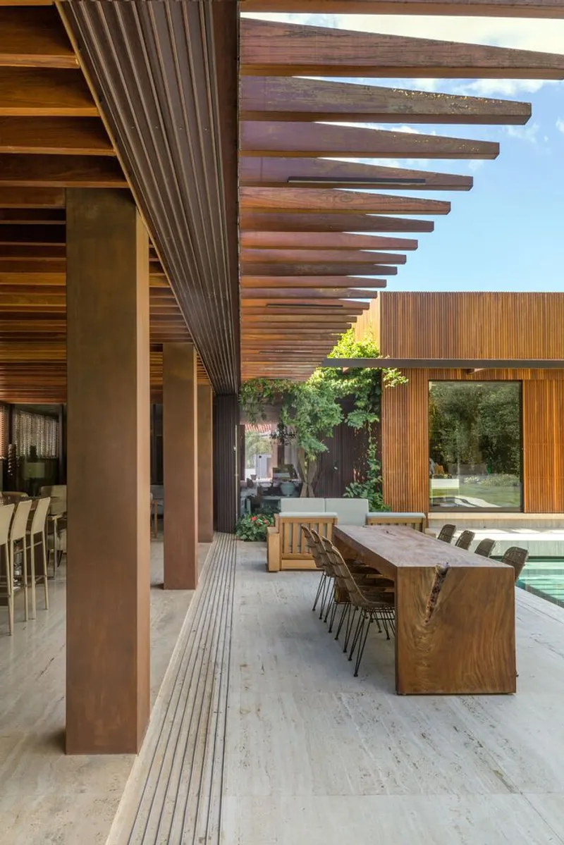 Slatted timber ceiling extending over outdoor terrace with steel columns and timber dining table