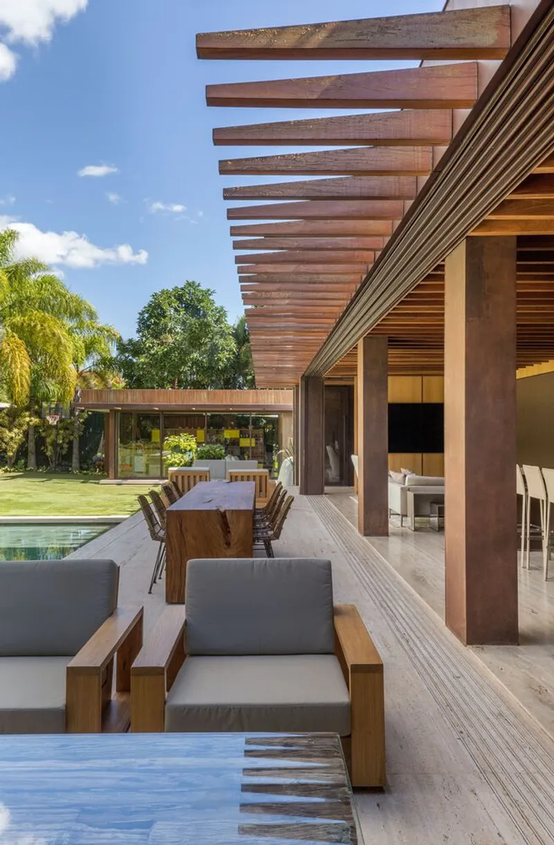 Outdoor terrace with spaced timber beams overhead and dining table adjacent to the pool