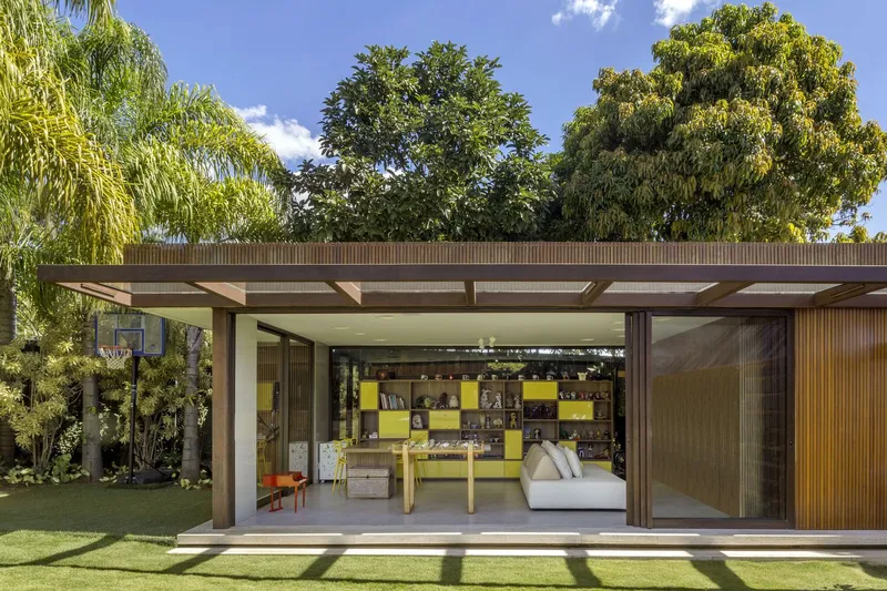 Garden pavilion with deep roof overhang and sliding glass walls opening to lawn under bright sky