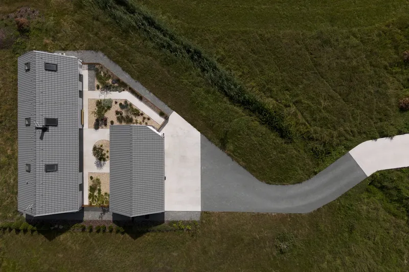 Aerial view of the L-shaped roof plan with planted courtyard and curved concrete path into the landscape