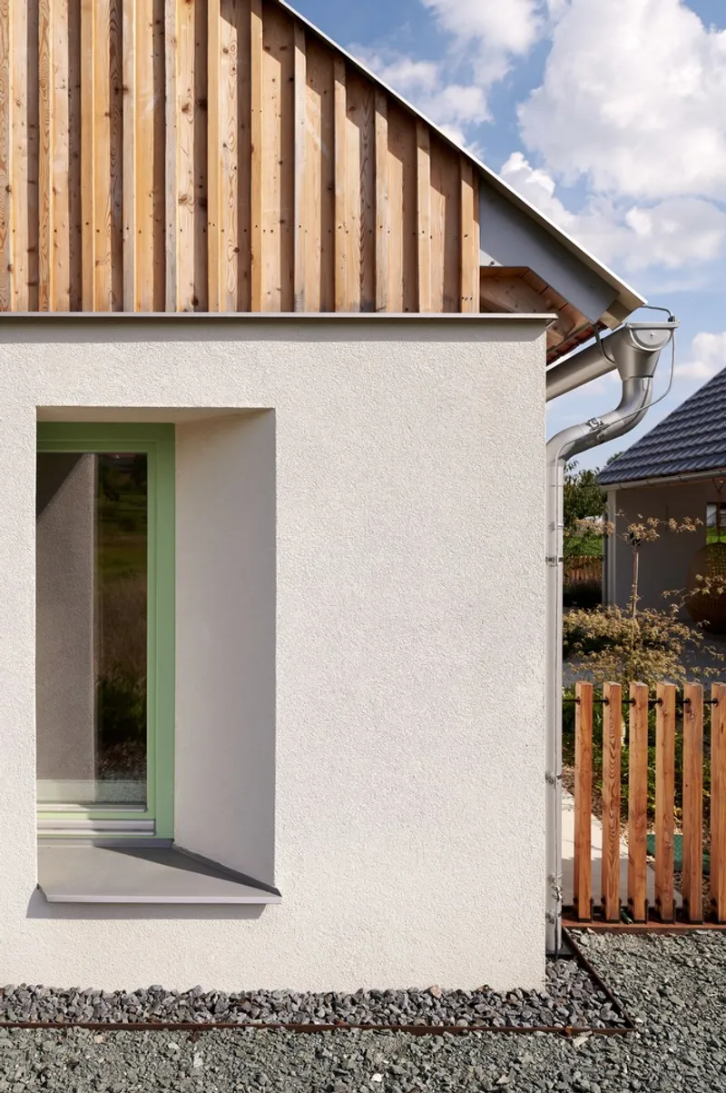 Corner detail of white rendered wall with recessed window and vertical timber cladding at the roof gable