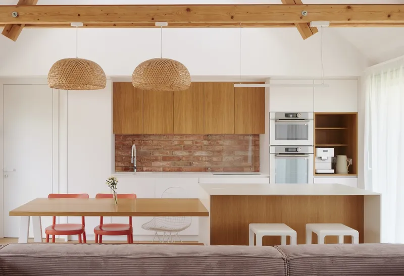 Open kitchen with timber upper cabinets, exposed brick backsplash and woven pendant lights above the island