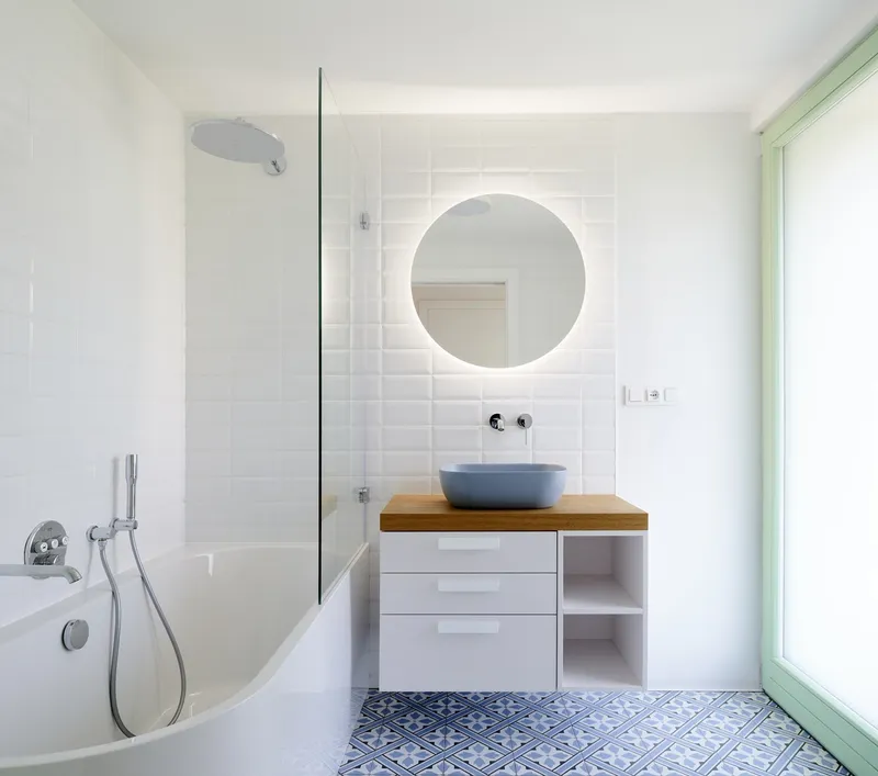 Bathroom with white subway tile wall, backlit round mirror and patterned blue floor tiles