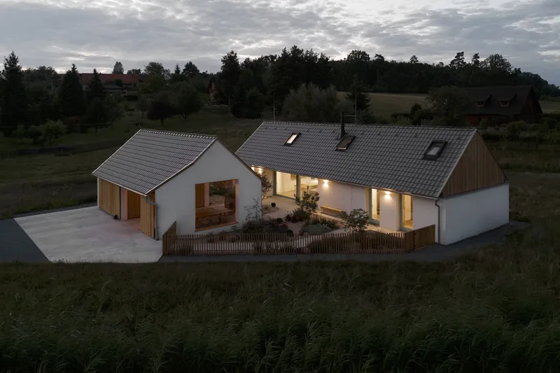 Aerial view of the illuminated linked gabled volumes with timber screening and concrete driveway at twilight