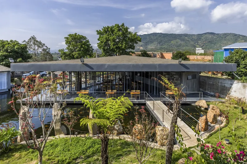 Elevated view of the flat concrete roof pavilion surrounded by a reflecting pond and planted garden with mountains beyond