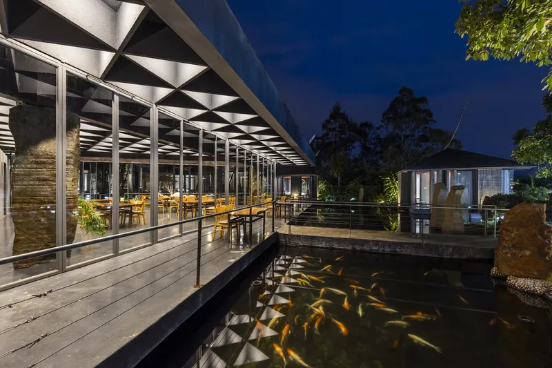 Evening view of the illuminated pavilion with geometric ceiling and koi pond in the foreground