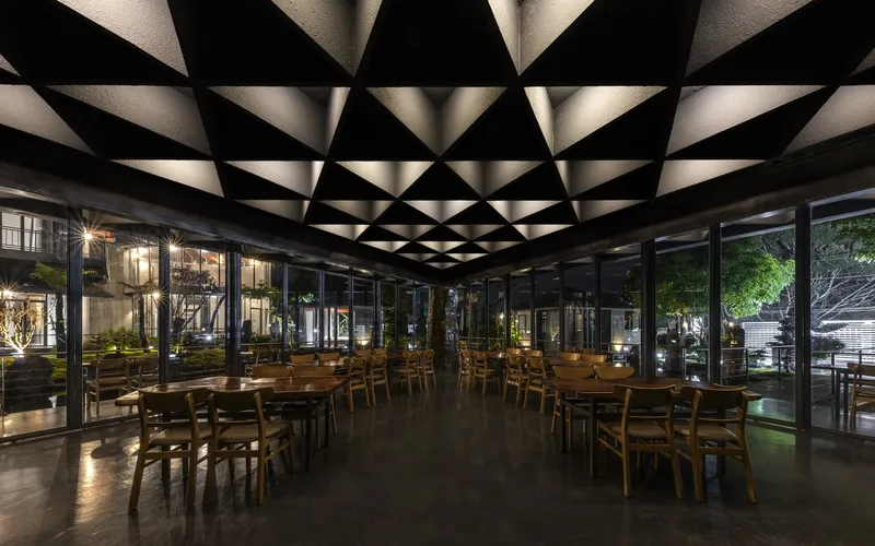 Interior dining hall with geometric coffered ceiling and floor-to-ceiling glazing at twilight