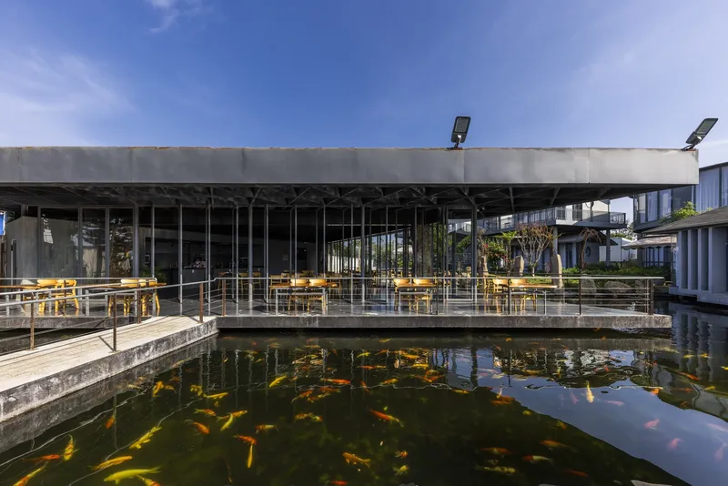 Covered outdoor terrace with concrete slab roof and yellow seating overlooking the reflecting koi pond